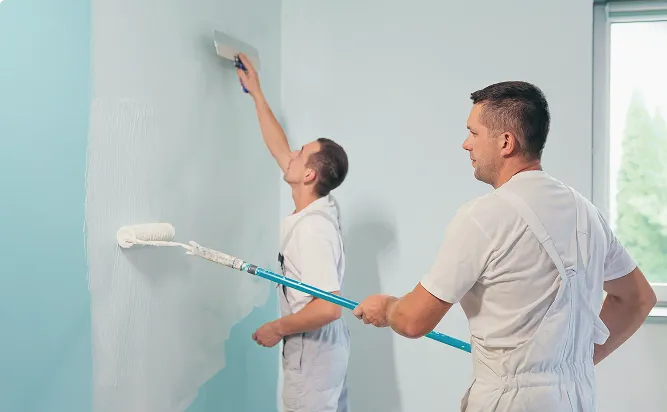 Zwei Maler streichen eine blaue Wand weiß.